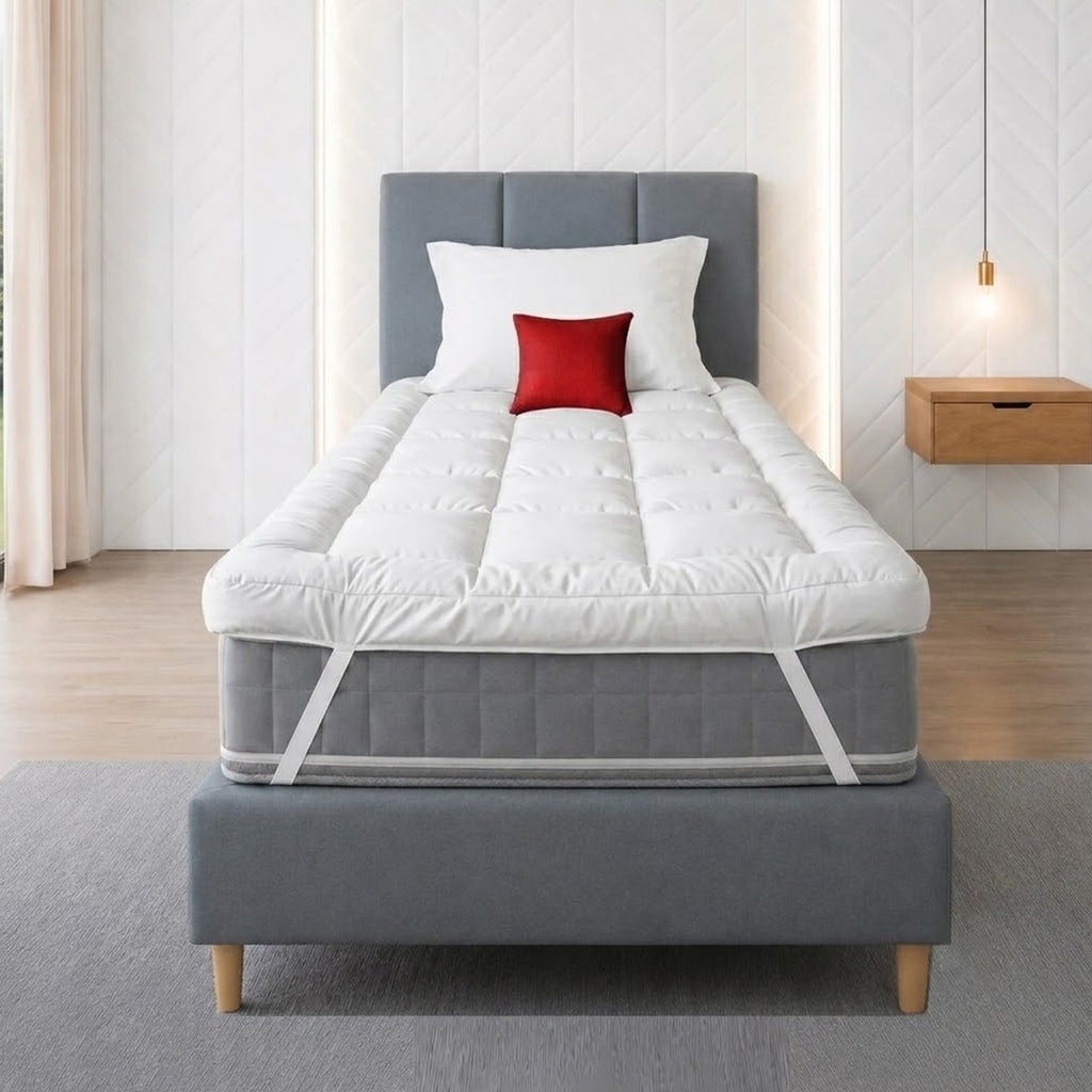 A white quilted mattress topper on a wooden bed frame, styled in a minimalist bedroom with a red pillow and a minimalist side table.