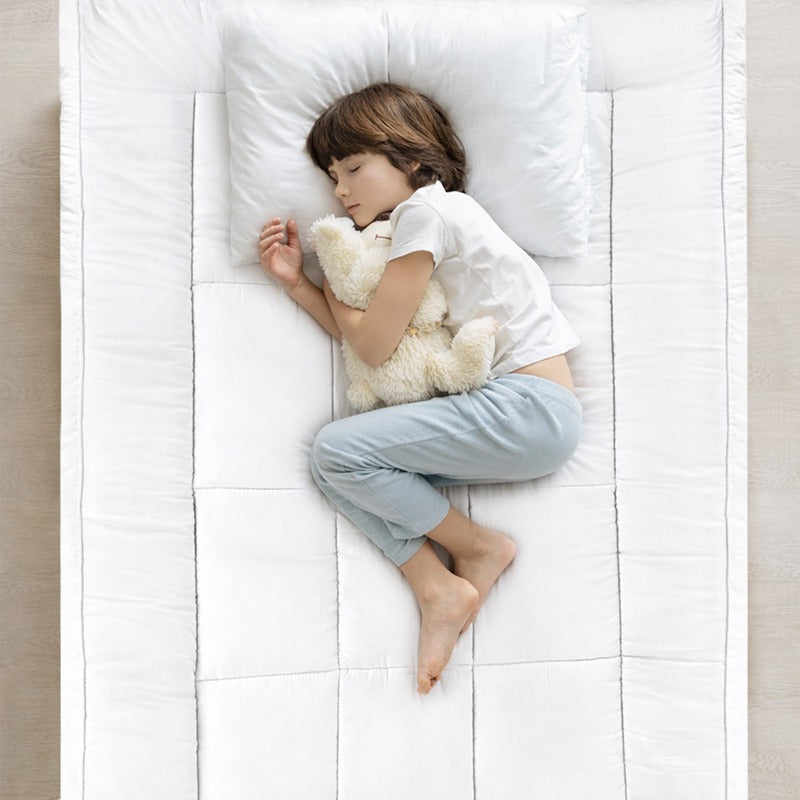 Child sleeping on a white mattress topper on single bed with a teddy bear