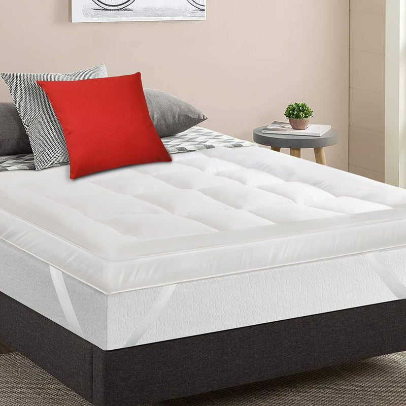White mattress topper on a bed with red and gray pillows in a bedroom setting.