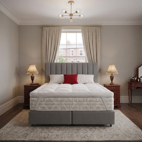 Grey bed with white mattress topper strapped to the off white mattress, red pillow, and wooden lamps on both sides of the bed in a bedroom setting.