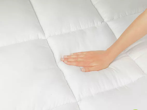 A hand is touching a soft mattress topper surface