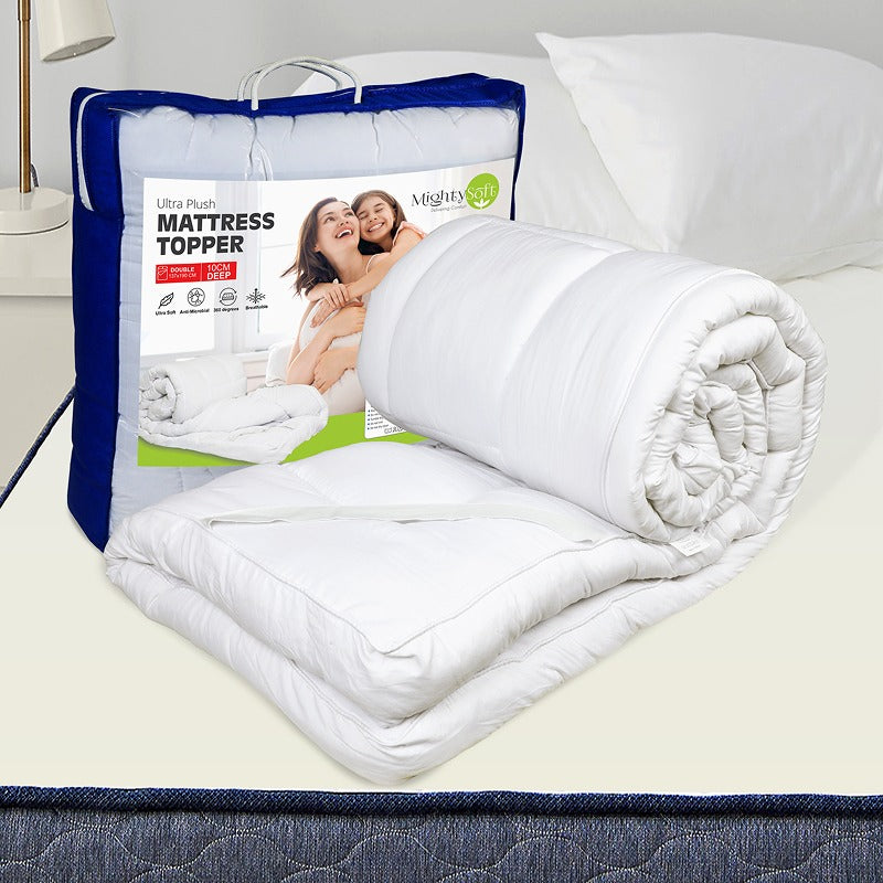 Roll of mattress topper on a bed with packaging displaying a family and product details.