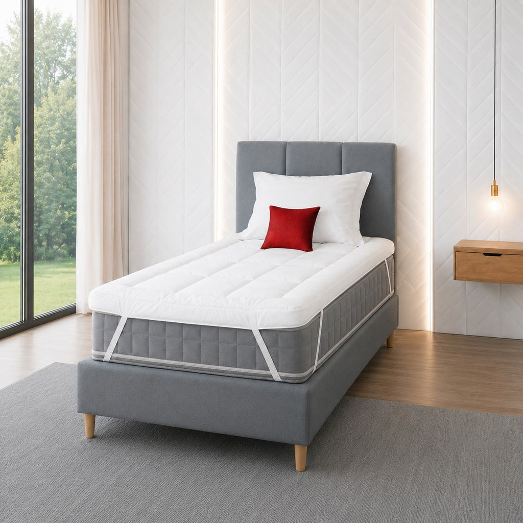 front left side view of a white bed topper elastically strapped to the mattress on a single bed.