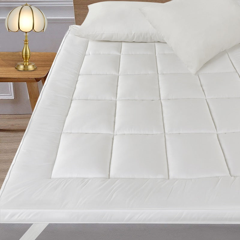 White quilted mattress topper on a bed with a lamp in the background