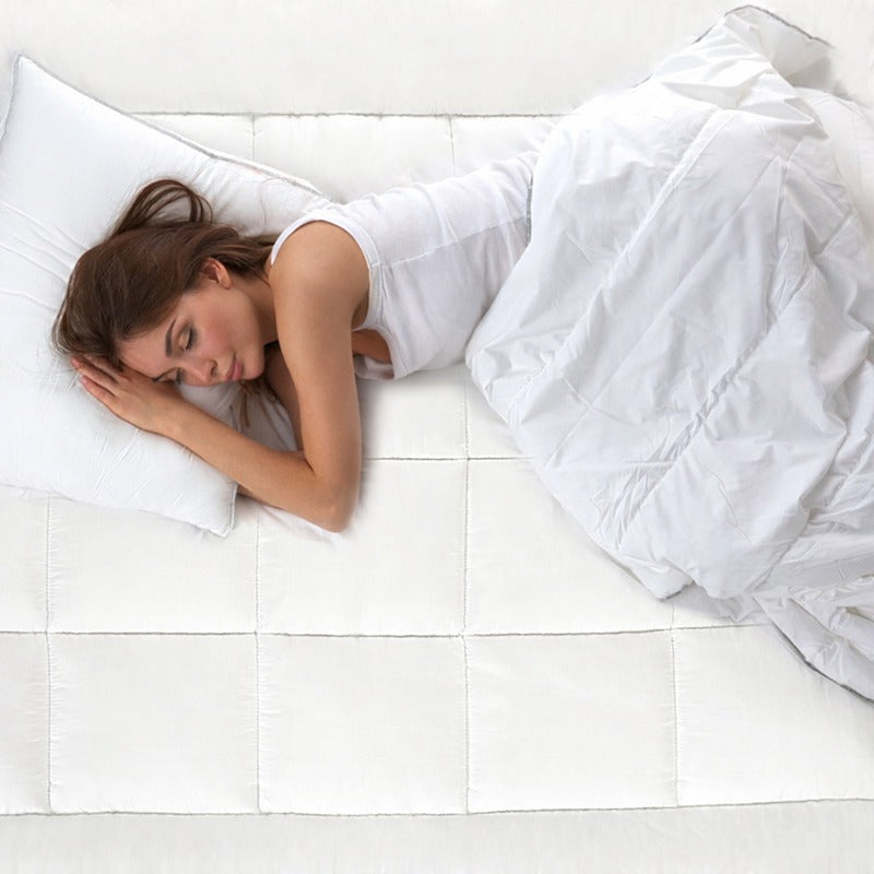 Woman sleeping peacefully under a white comforter on a bed with white mattress topper.